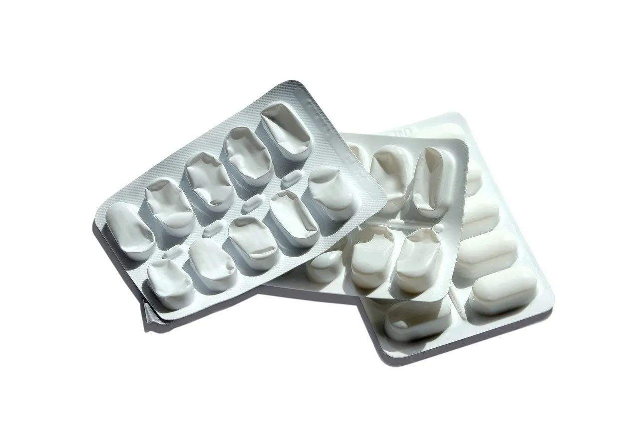 Drei übereinanderliegende Blisterpackungen mit weißen ovalen Tabletten, die obere ist leer und hat eingedrückte Mulden